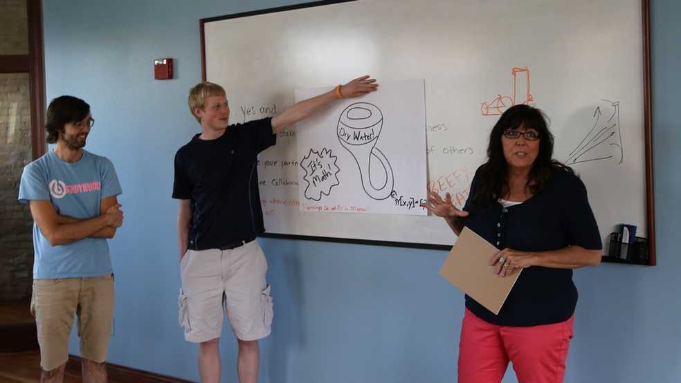 Three people standing in front of a whiteboard. They are explaining a picture.