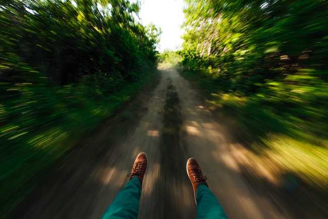 Point of view photo with legs extending from behind the camera, there's a wooded path in front of you and the camera blur suggest rapid movement
